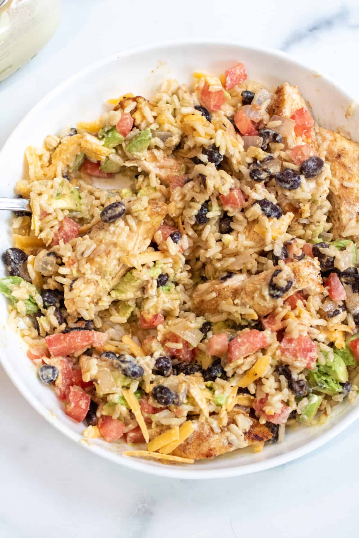 a big bowl of all mixed up rice bowl with sauce, tomatoes, beans, chicken, and cheese and avocado.