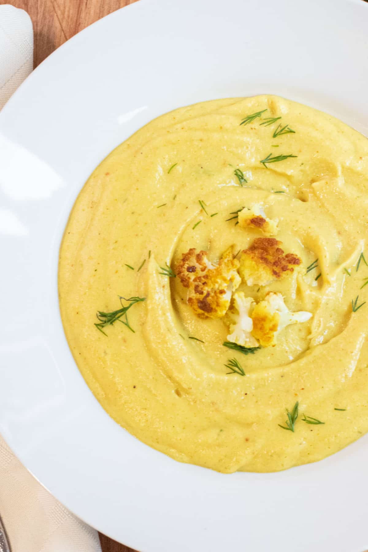 an overhead of a bowl of yellow creamy soup with cauliflower on top and dill.