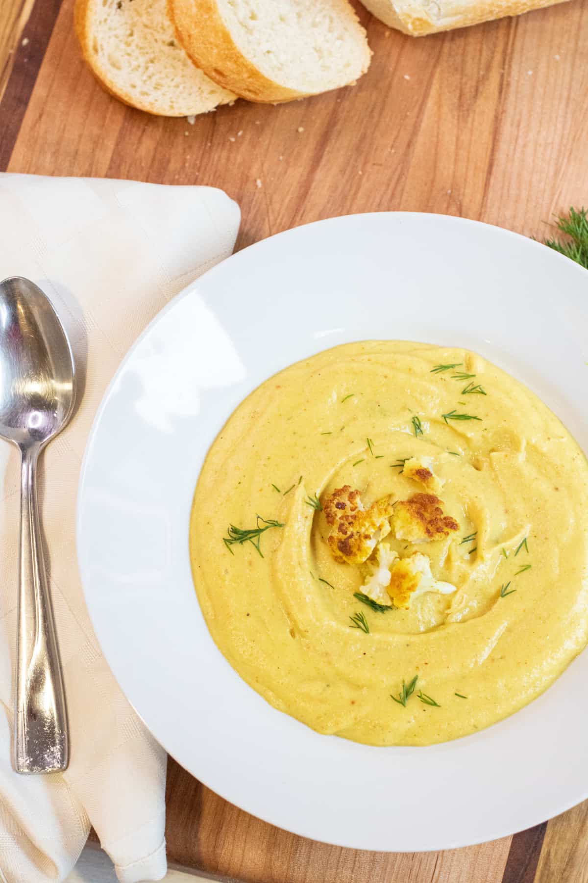 an overhead of a bowl of yellow creamy soup with cauliflower on top and dill.