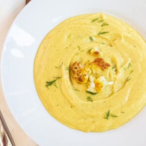 an overhead of a bowl of yellow creamy soup with cauliflower on top and dill.