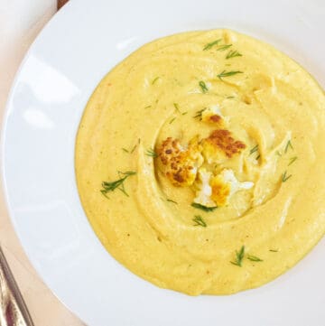 an overhead of a bowl of yellow creamy soup with cauliflower on top and dill.