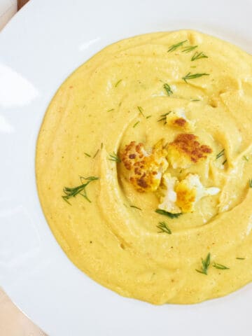 an overhead of a bowl of yellow creamy soup with cauliflower on top and dill.