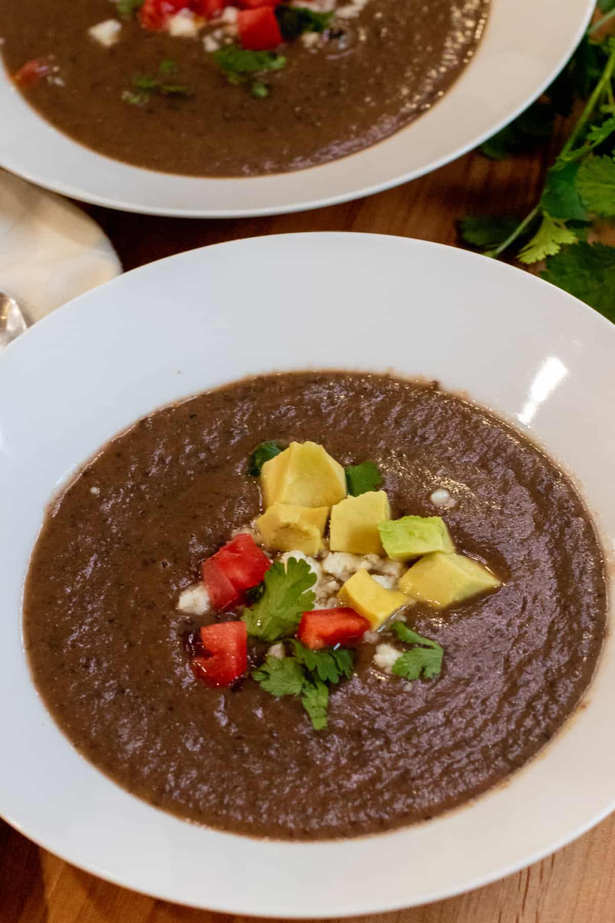 a bowl of black bean soup topped with avocado, cheese, and diced tomatoes.