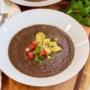 a bowl of black bean soup topped with avocado, cheese, and diced tomatoes.