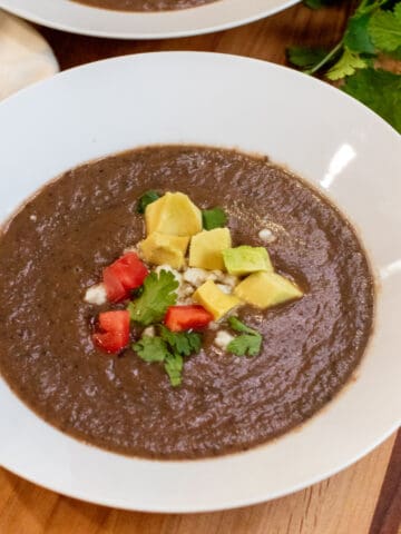 a bowl of black bean soup topped with avocado, cheese, and diced tomatoes.