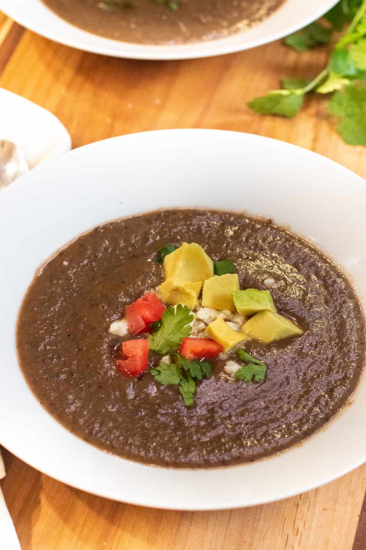 a bowl of black bean soup topped with avocado, cheese, and diced tomatoes.