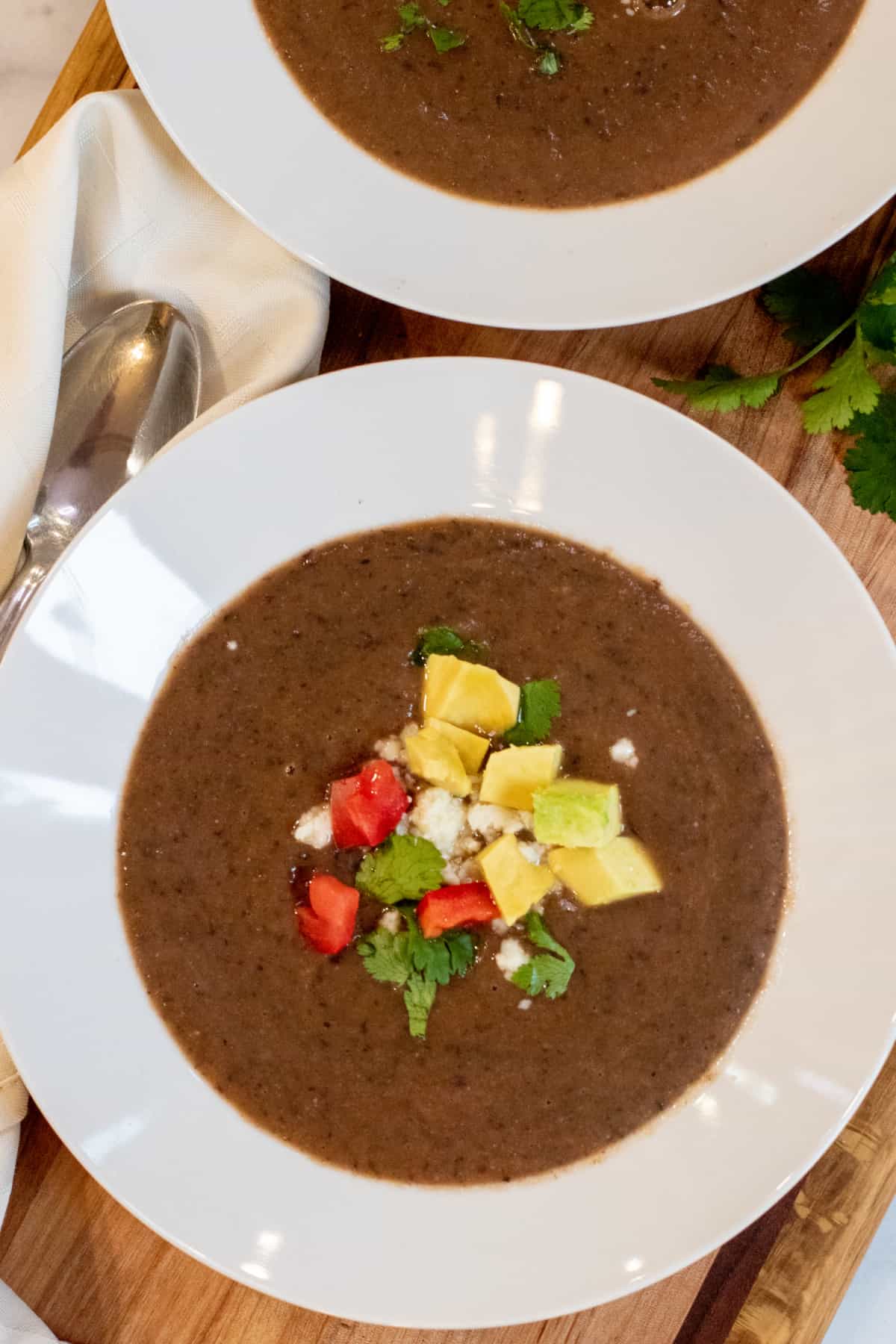 a bowl of black bean soup topped with avocado, cheese, and diced tomatoes.