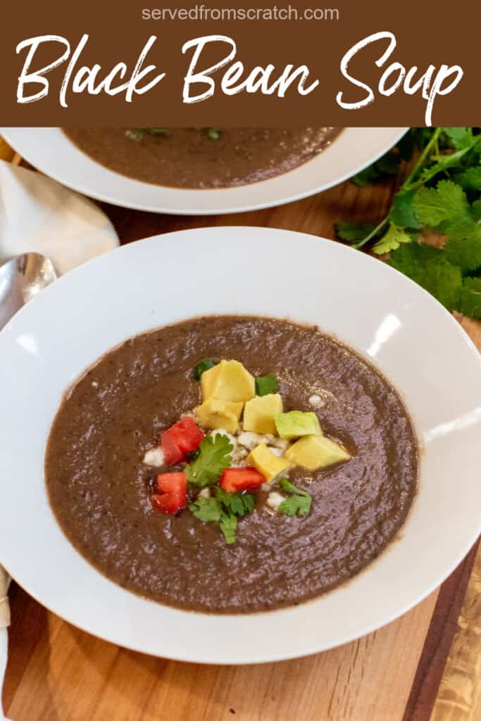 a bowl of black bean soup topped with avocado, cheese, and diced tomatoes with Pinterest pin text.