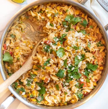 an overhead of a pan of pasta with cilantro, cheese, corn and a creamy sauce.