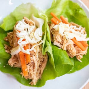 a plate of lettuce wraps with shredded chicken topped with carrots and cabbage.