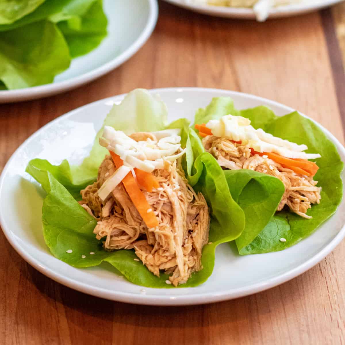 a plate of lettuce wraps with shredded chicken topped with carrots and cabbage.