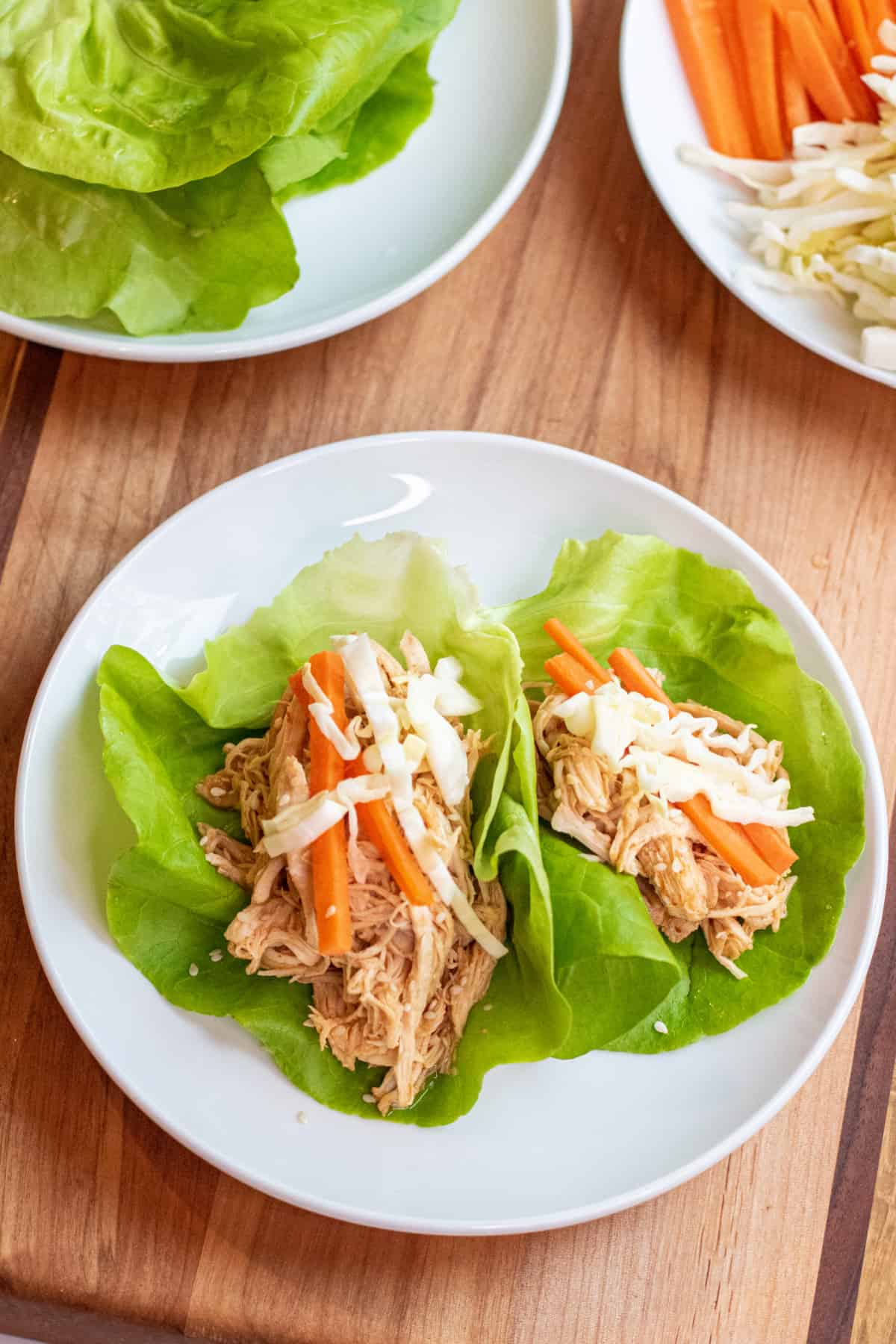 a plate of lettuce wraps with shredded chicken topped with carrots and cabbage.