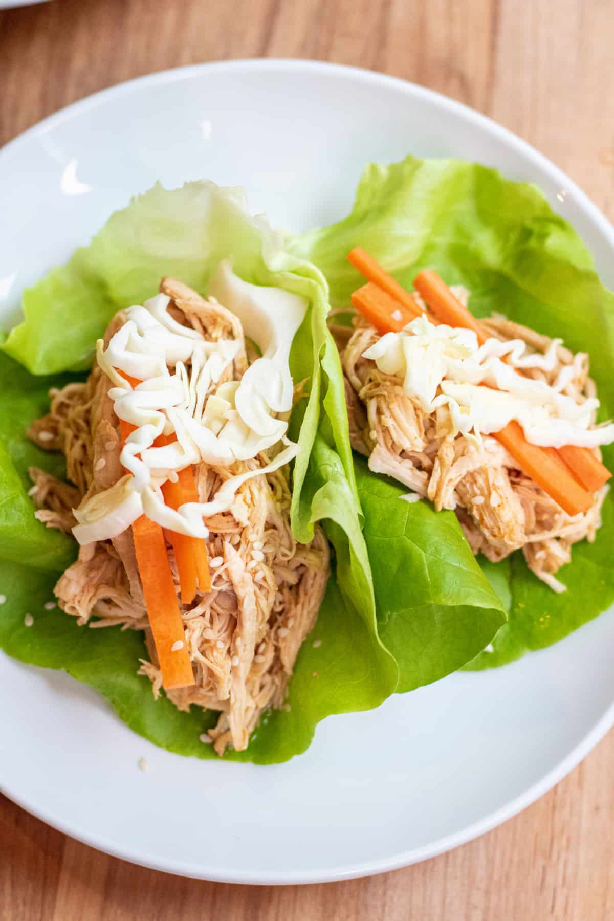 a plate of lettuce wraps with shredded chicken topped with carrots and cabbage.