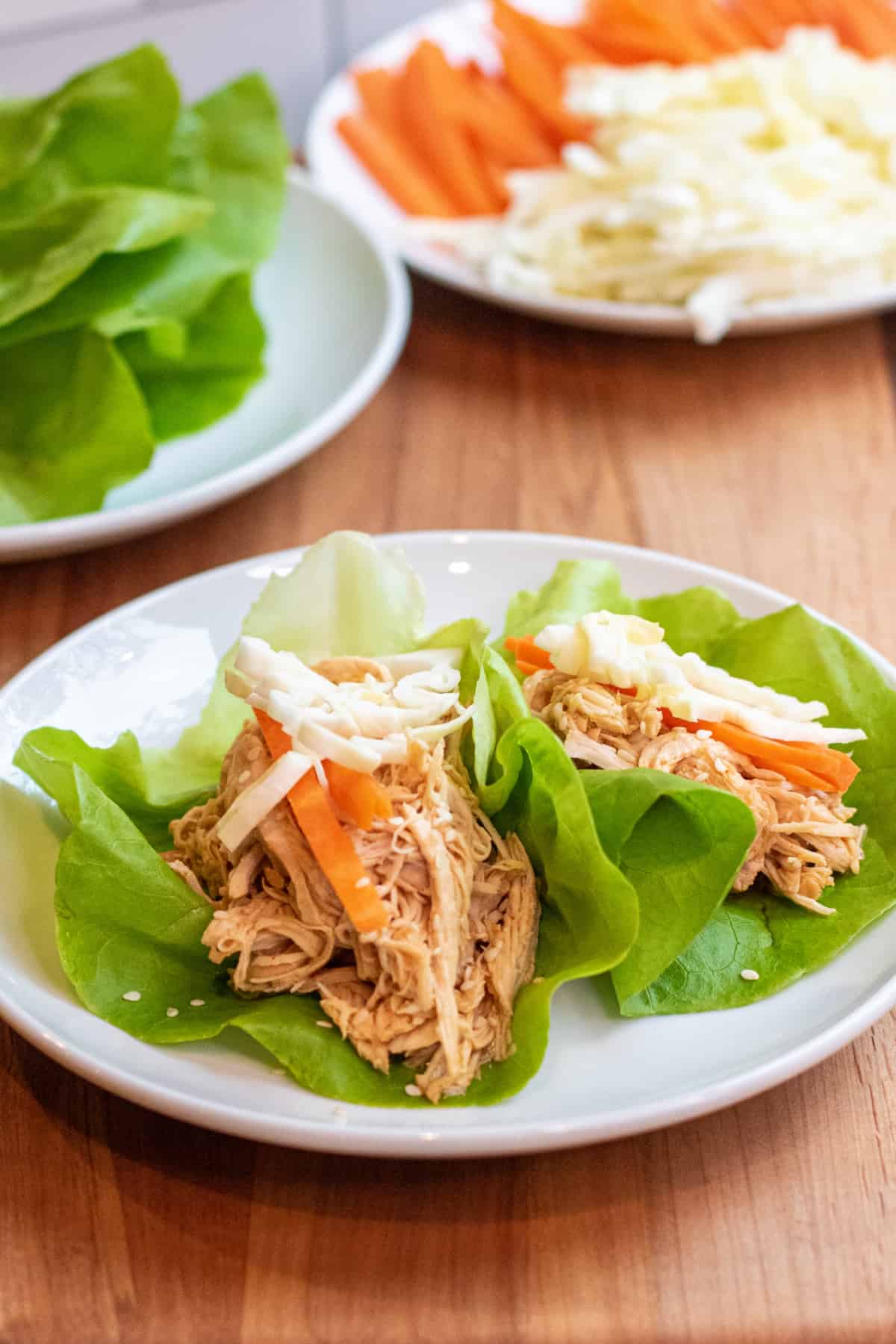 a plate of lettuce wraps with shredded chicken topped with carrots and cabbage.