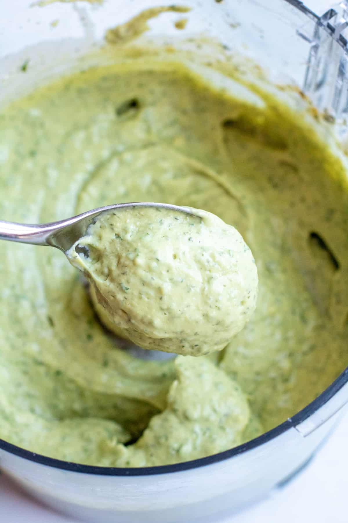 a spoon of creamy dressing from a bowl of green dressing.