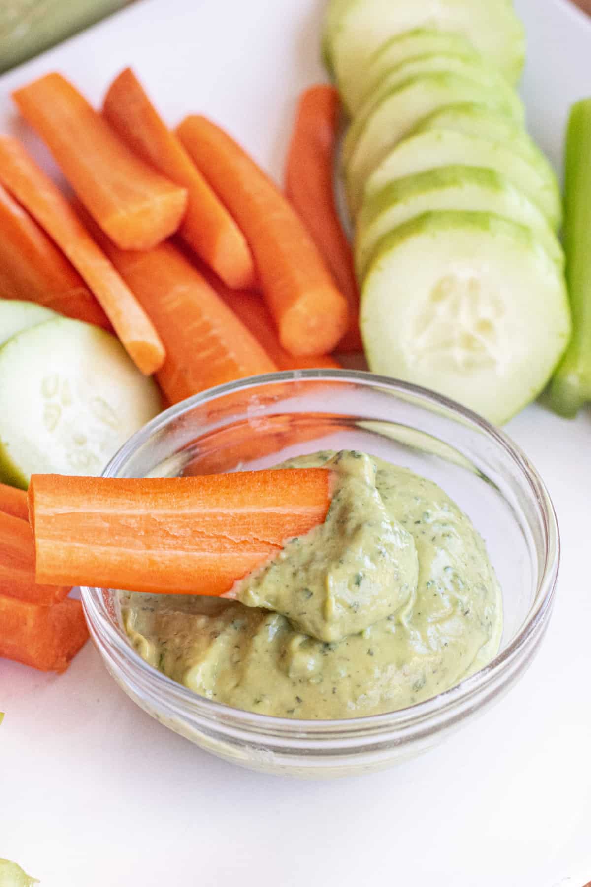 a carrot being dipped into a bowl of green dip on a plate of veggies.