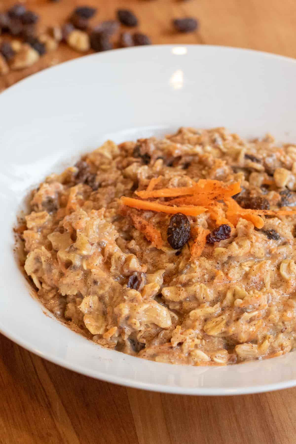 a bowl of oatmeal with shredded carrots and raisins on top.