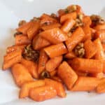 a plate of glazed carrots with walnuts.