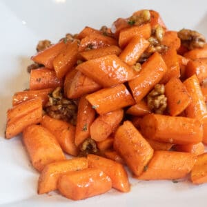 a plate of glazed carrots with walnuts.