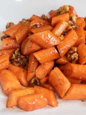 a plate of glazed carrots with walnuts.