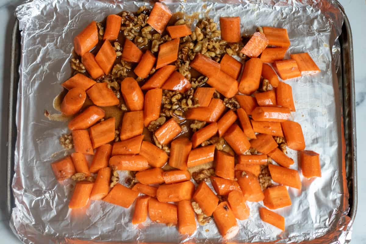 a foil lined baking sheet with carrots and walnuts glazed.