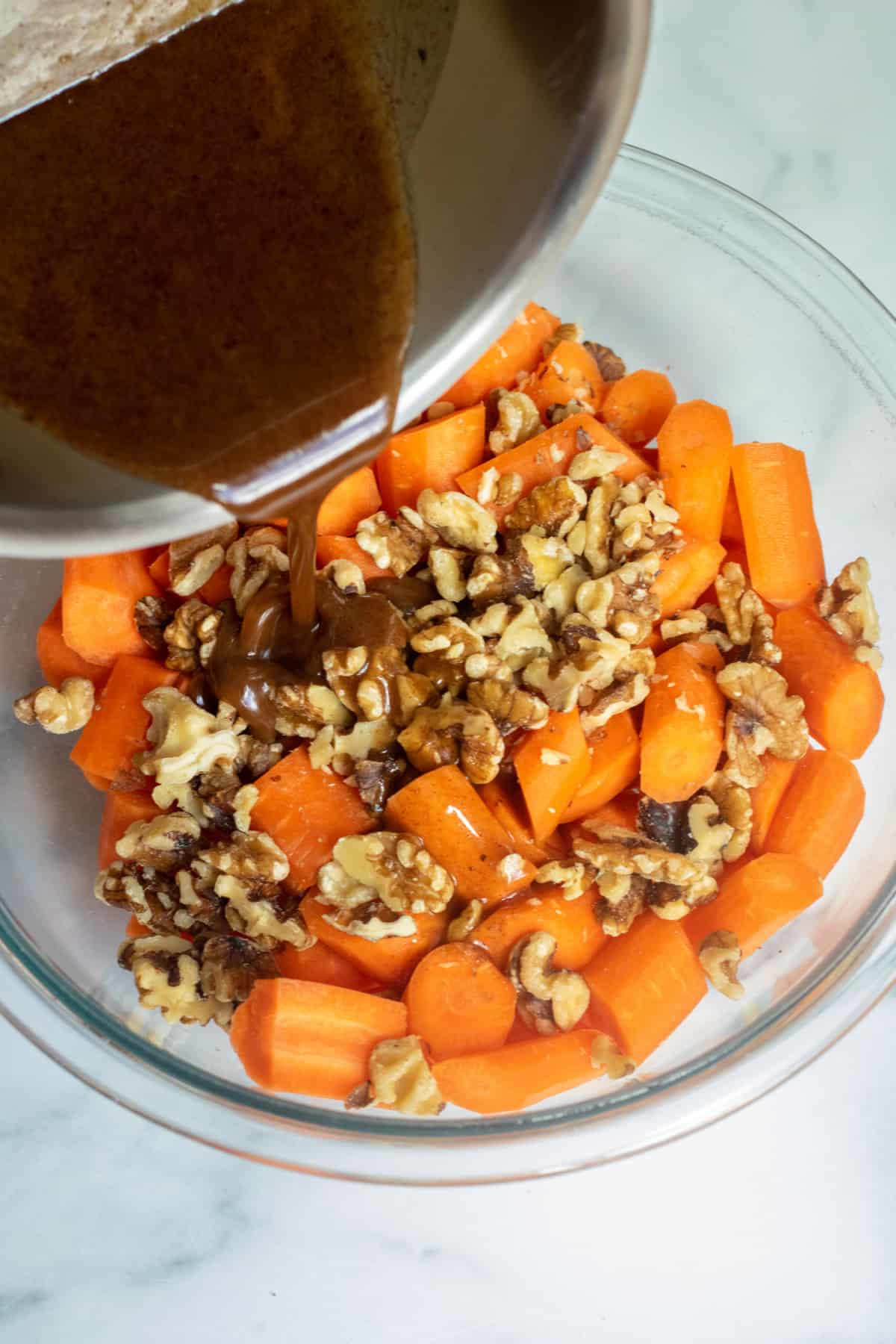 syrup being poured into a bowl of cut carrots and walnuts.