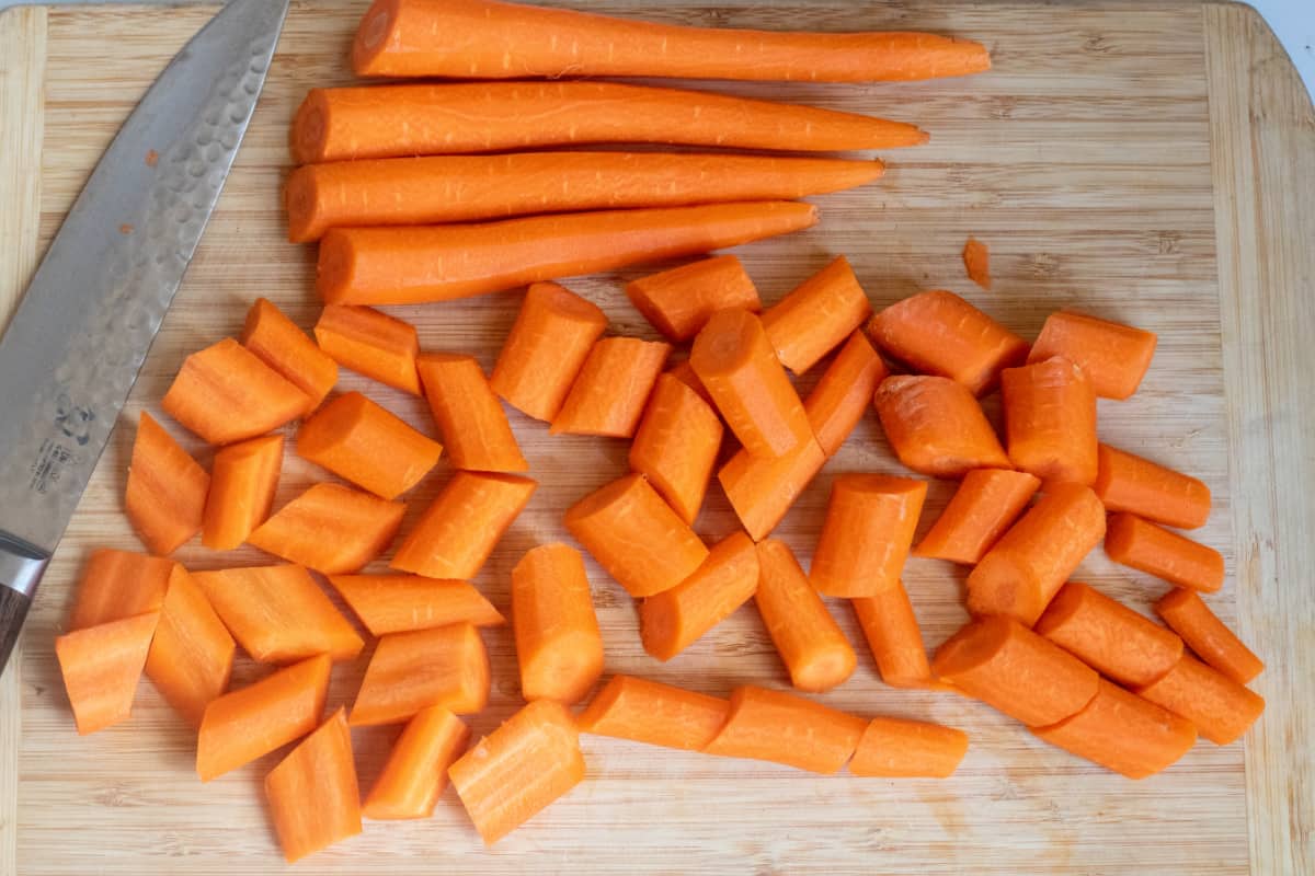 a cutting board with whole peeled carrots and a knife and them cut up.