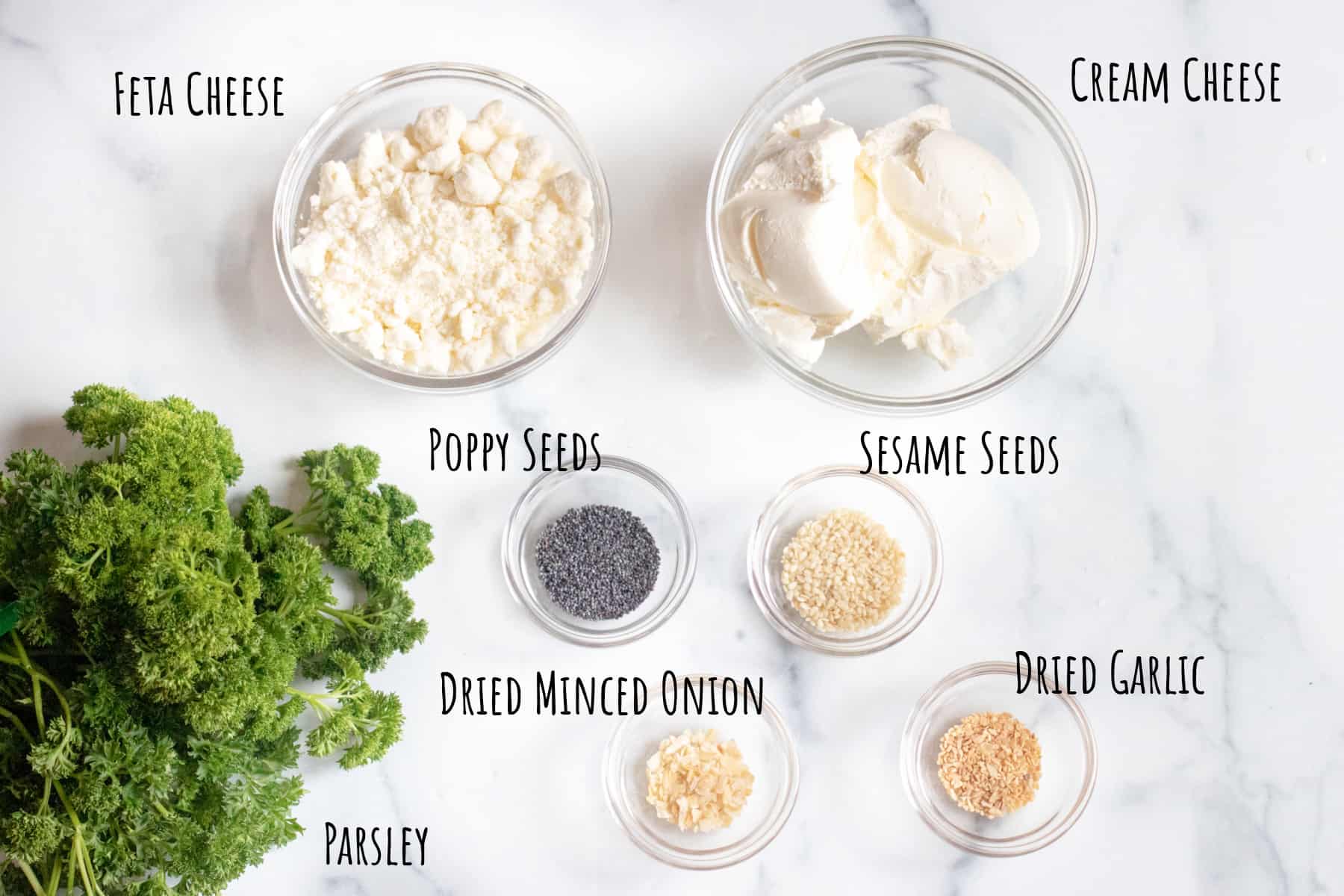 bowls of feta, cream cheese, poppy seeds, sesame seeds, garlic, and onion with fresh parsley.
