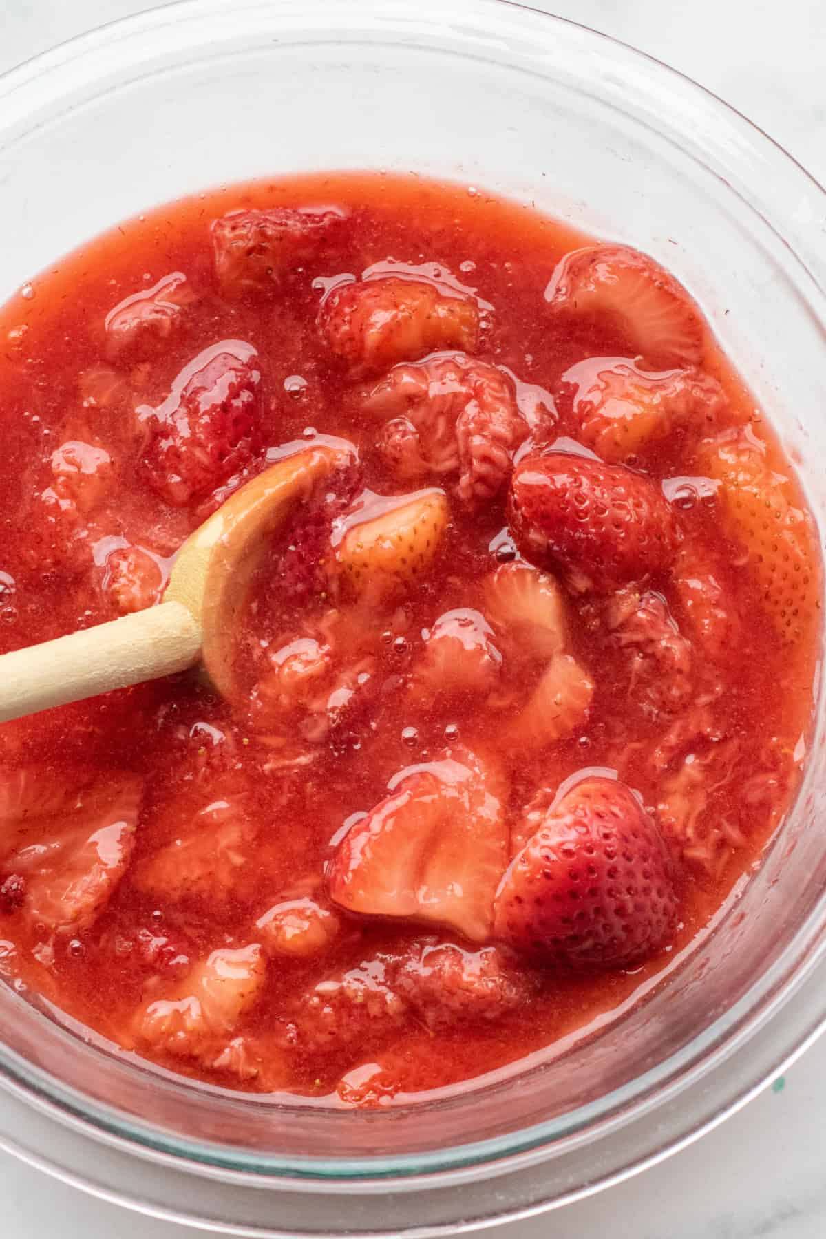 a bowl of strawberry compote with a wooden spoon in it.