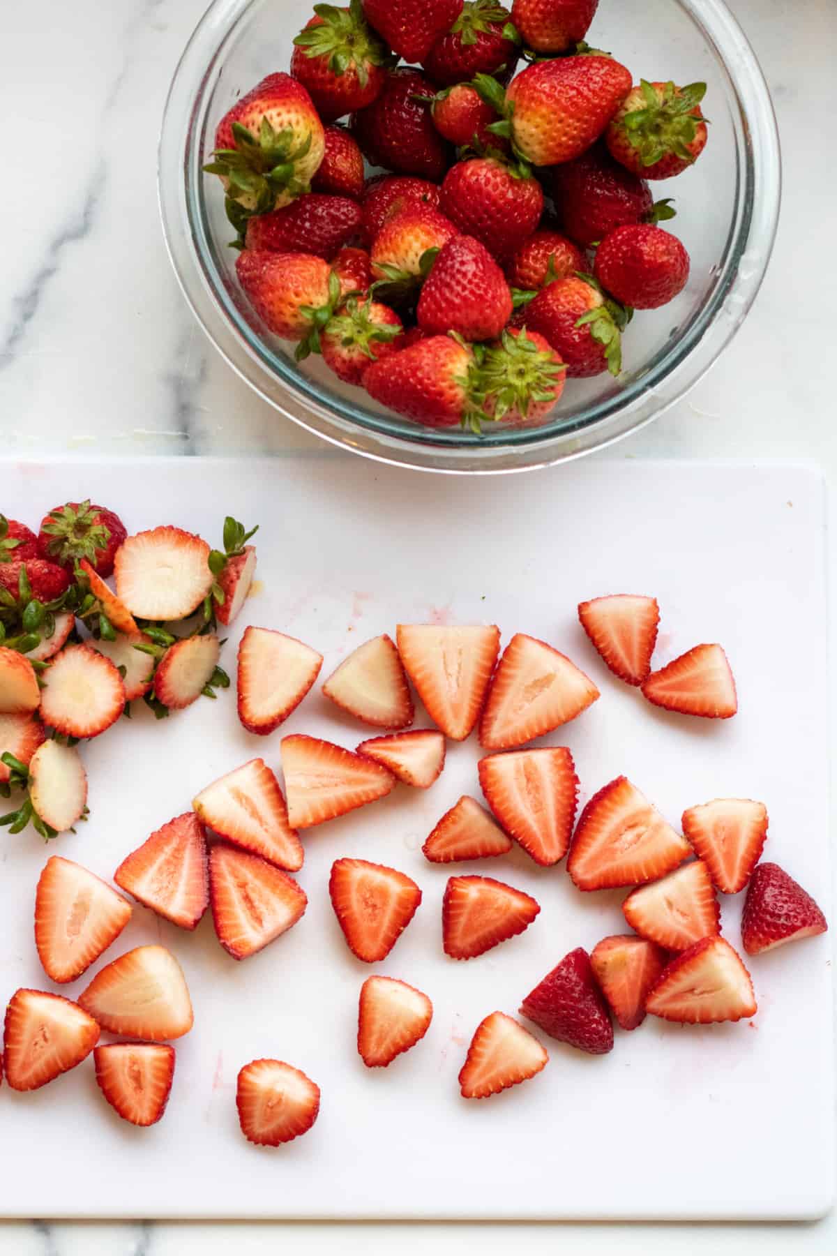 a bowl of fresh strawberries and a cutting board with strawberries cut.