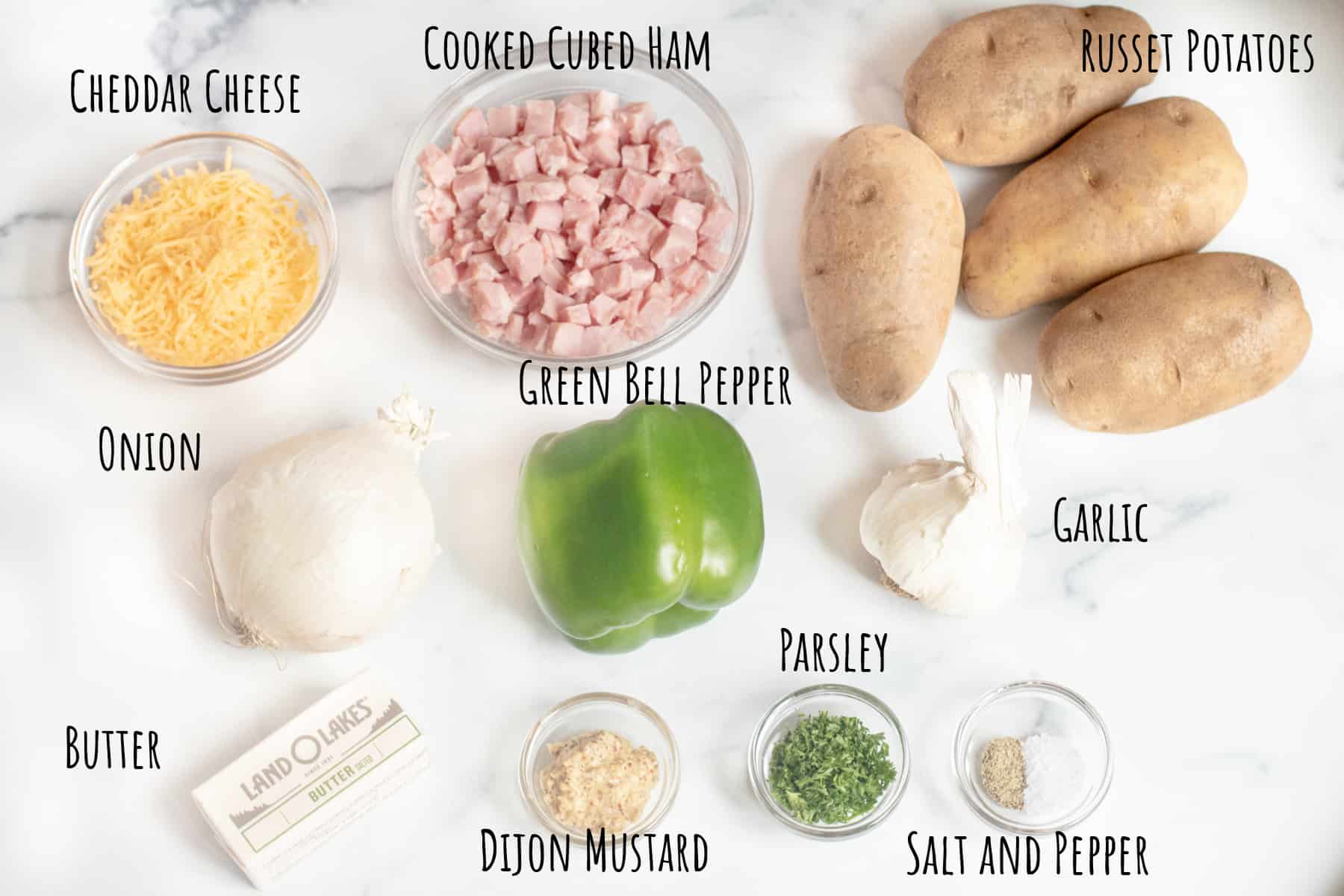 potatoes, cheese, ham, onion, bell pepper, garlic, butter, spices on a counter.