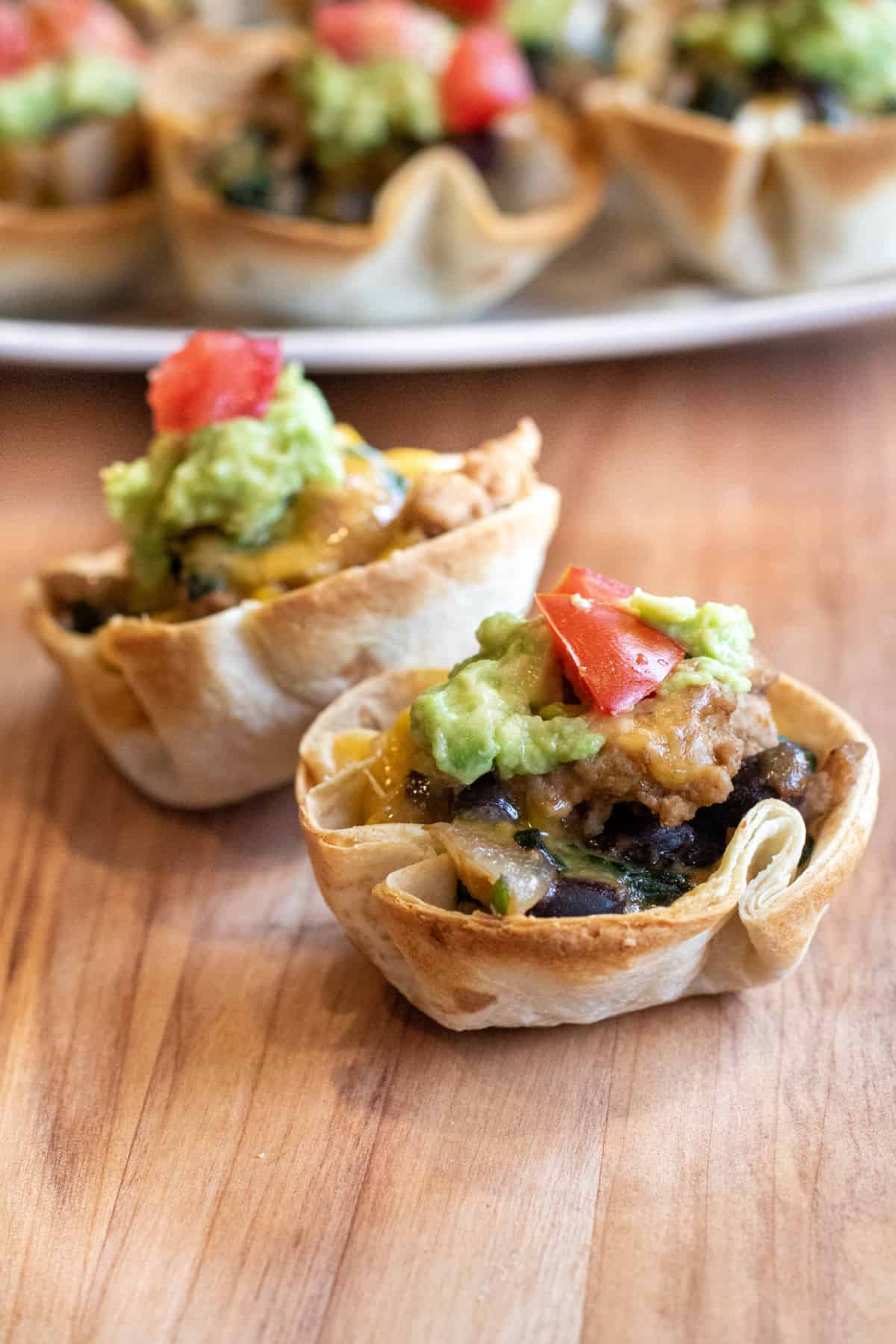 two little taco cups topped with guacamole and tomatoes.