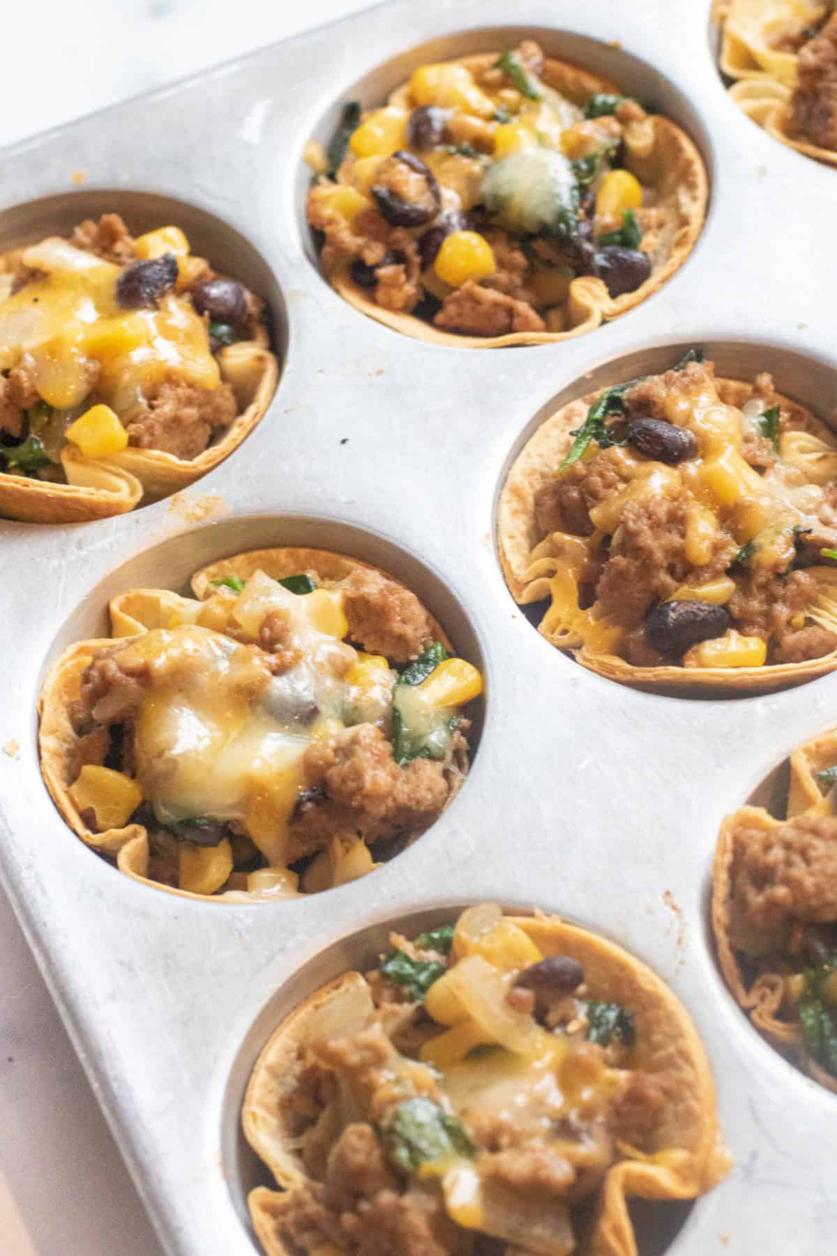 a muffing pan with taco cups and melted cheese.