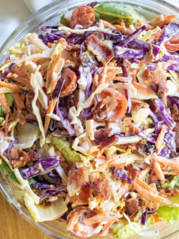 a bowl of coleslaw with bacon tomatoes and some lettuce.