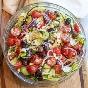 a bowl of zucchini salad with tomatoes, olives, onions and feta.