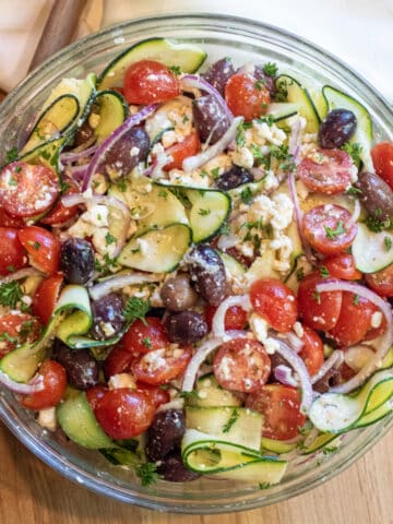 a bowl of zucchini salad with tomatoes, olives, onions and feta.