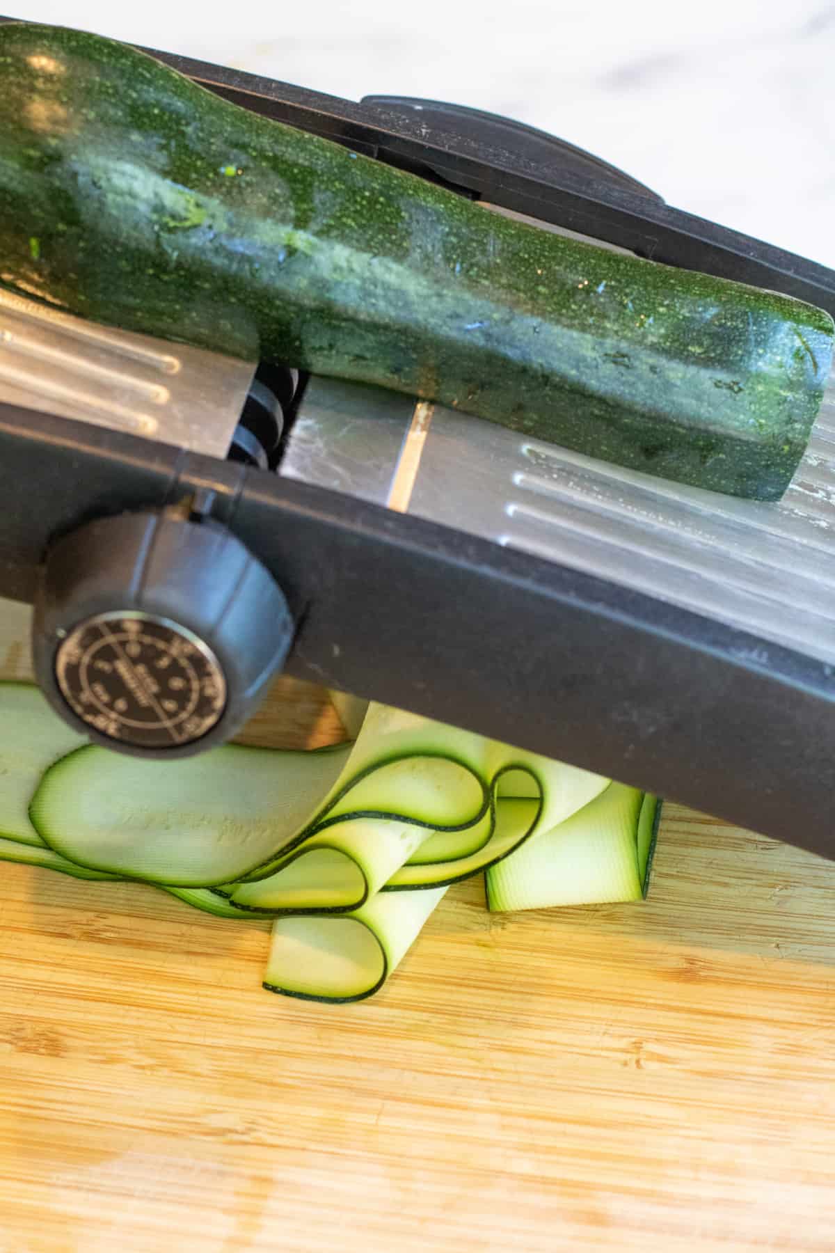 zucchini being sliced with a mandoline.
