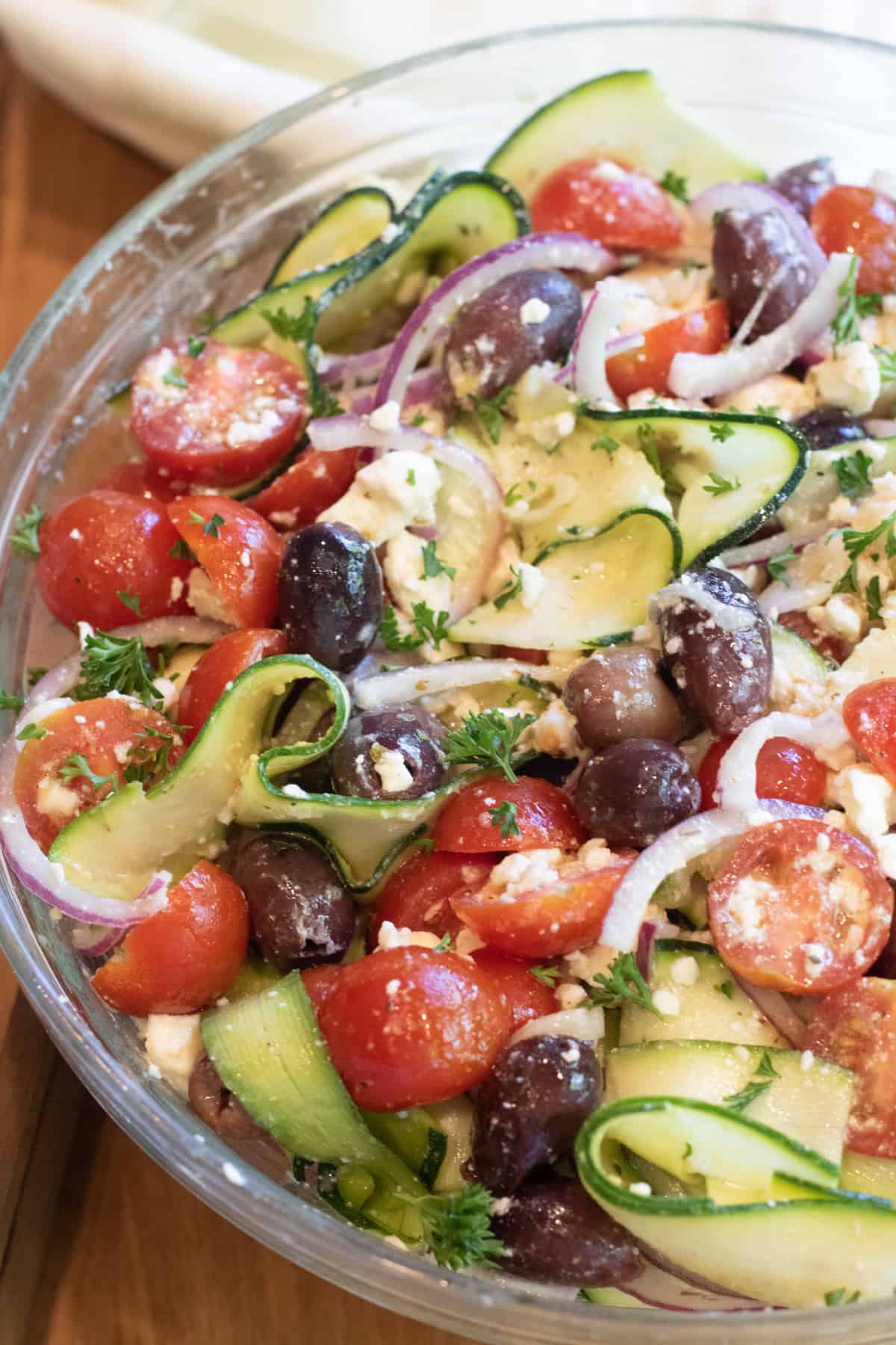 a bowl of zucchini salad with tomatoes, olives, onions and feta.
