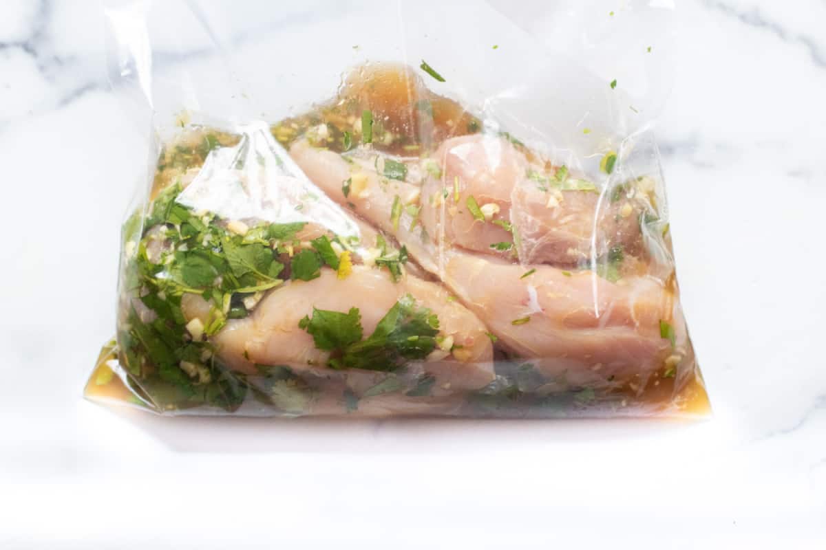 raw chicken marinating in a bag with cilantro.