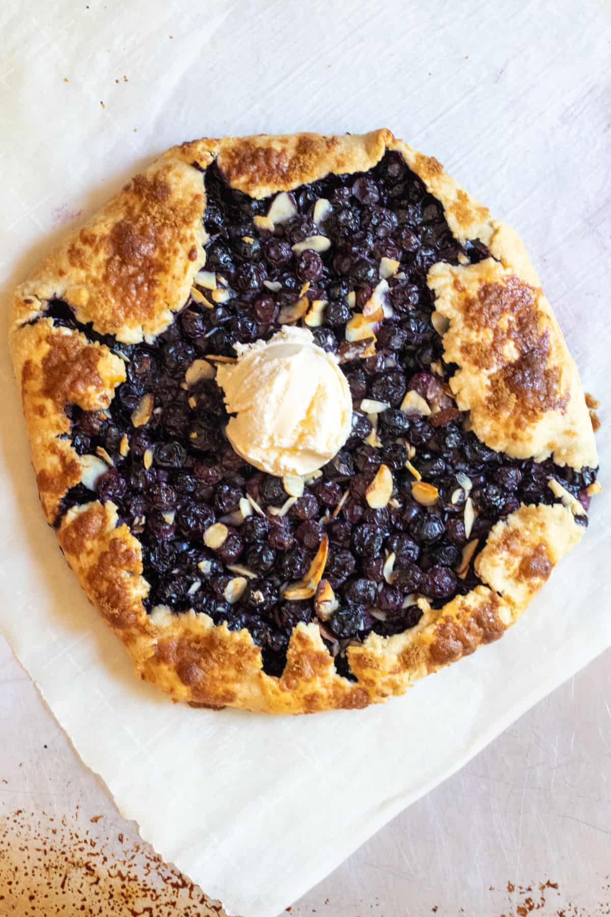 an overhead of a baked blueberry galette with almonds with ice cream.