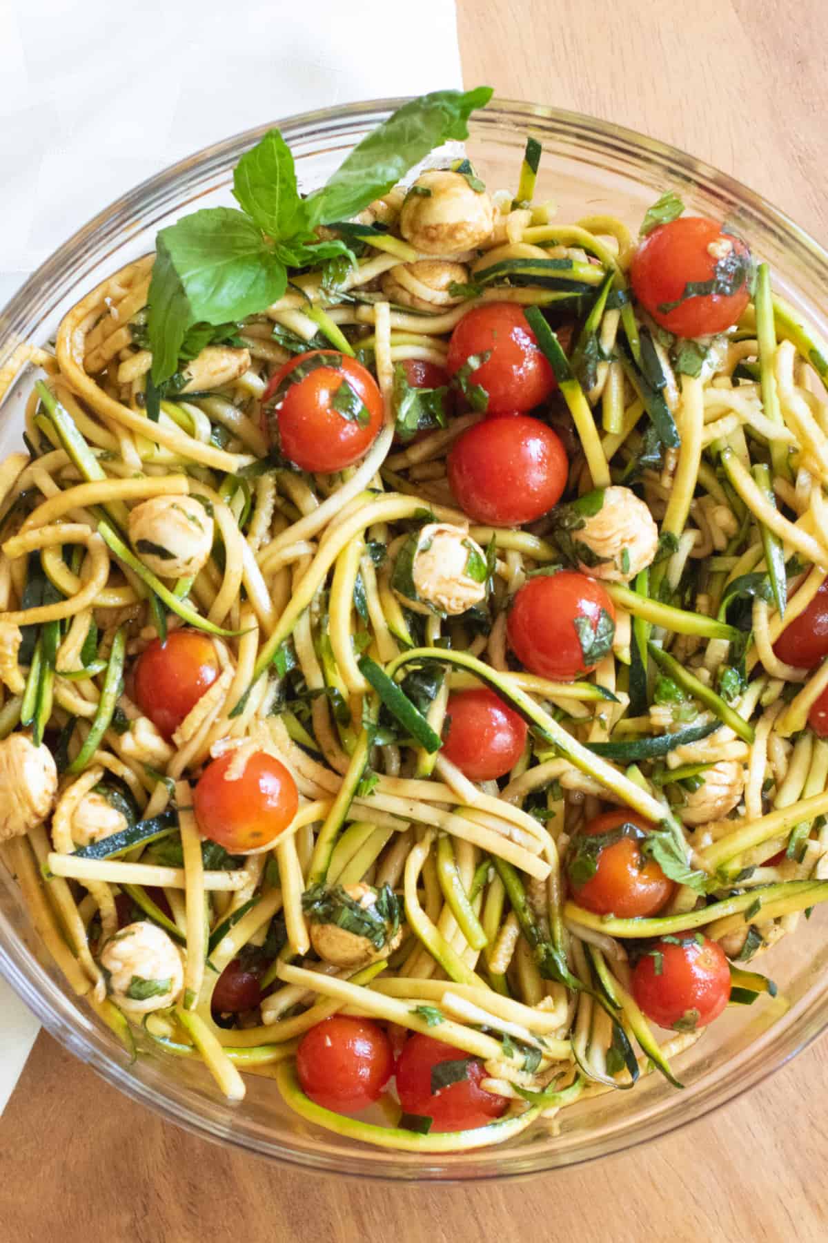 a bowl of zucchini noodles with tomatoes, mozzarella, basil, and balsamic dressing.