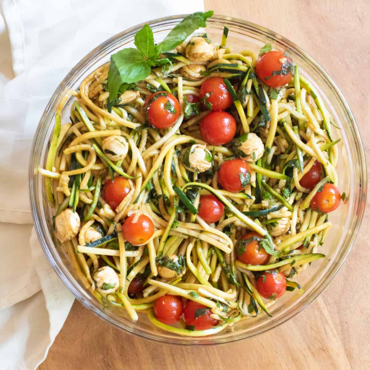 a bowl of zucchini noodles, cherry tomatoes and mozzarella balls with a balsamic dressing.