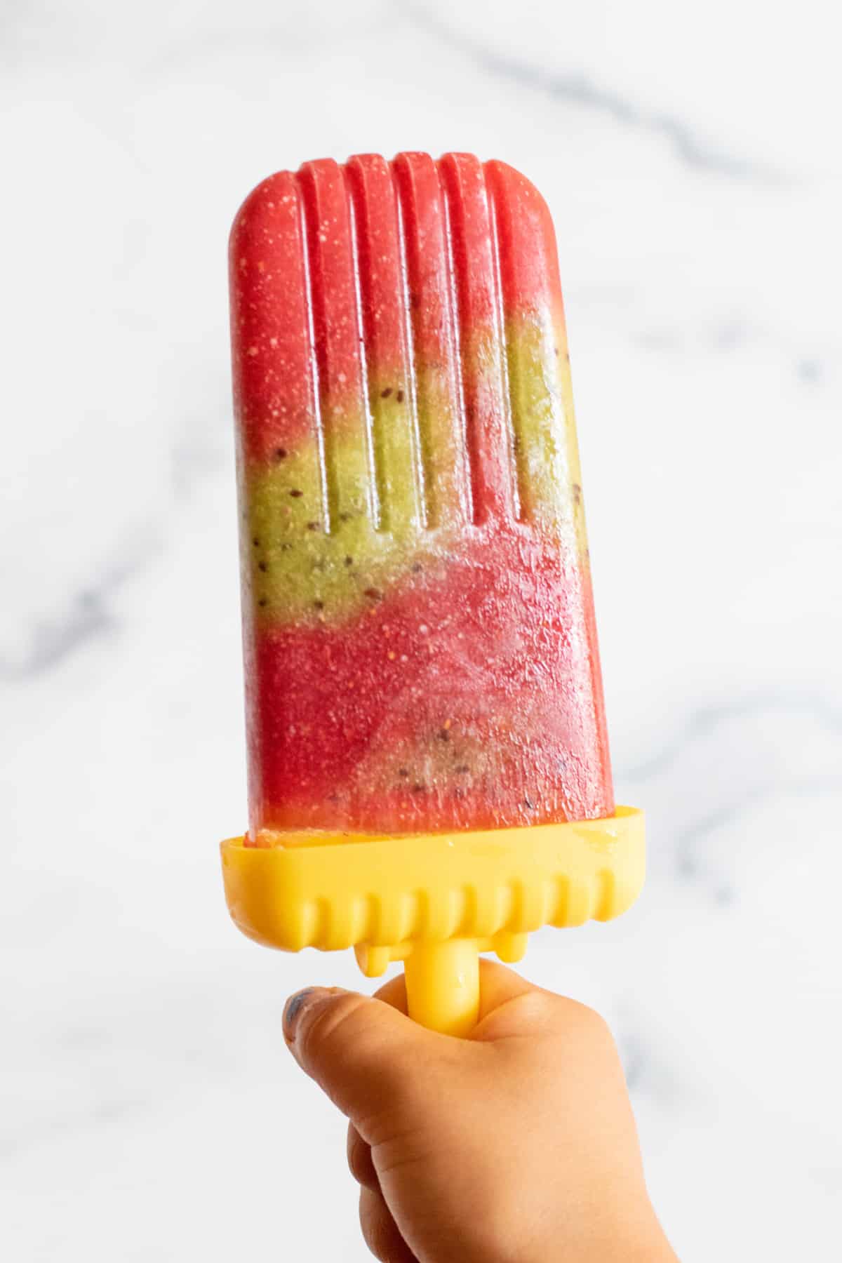 a strawberry and kiwi popsicle held by a hand.