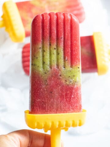a strawberry and kiwi popsicle held by a hand.
