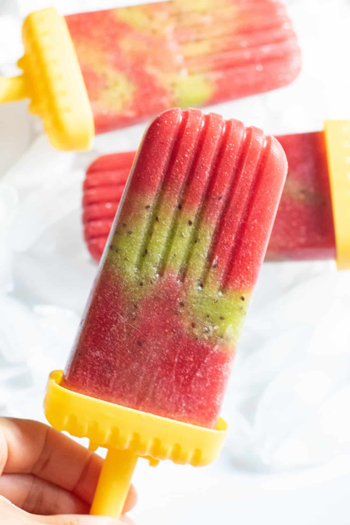 a strawberry and kiwi popsicle held by a hand.