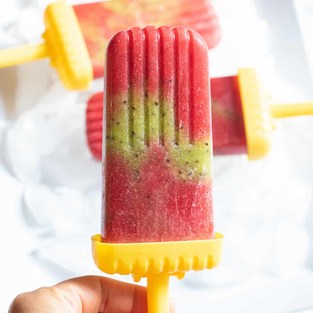 a strawberry and kiwi popsicle held by a hand.