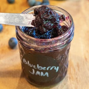a mason jar labeled Blueberry jam and a knife taking some out.