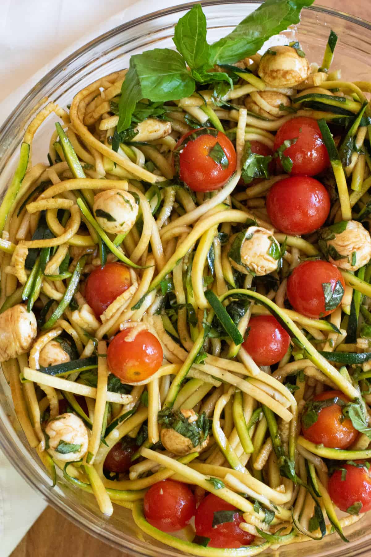 a bowl of zucchini noodles with tomatoes, mozzarella, basil, and balsamic dressing.