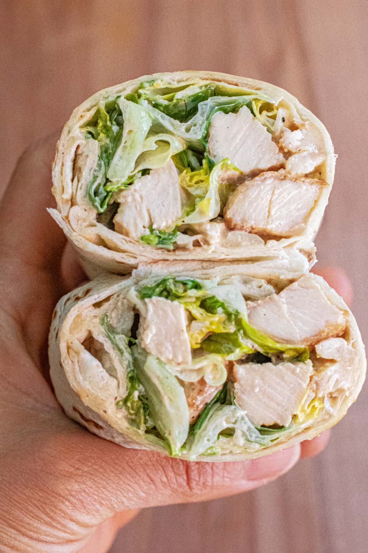 a hand holding a halved chicken caesar salad wrap.