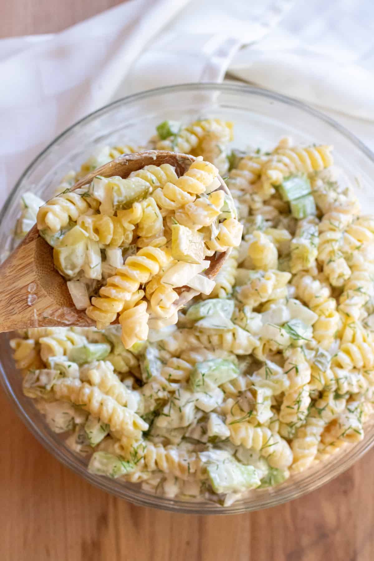 an overhead bowl of rotini pasta salad with celery and dill pickle and a wooden spoon.